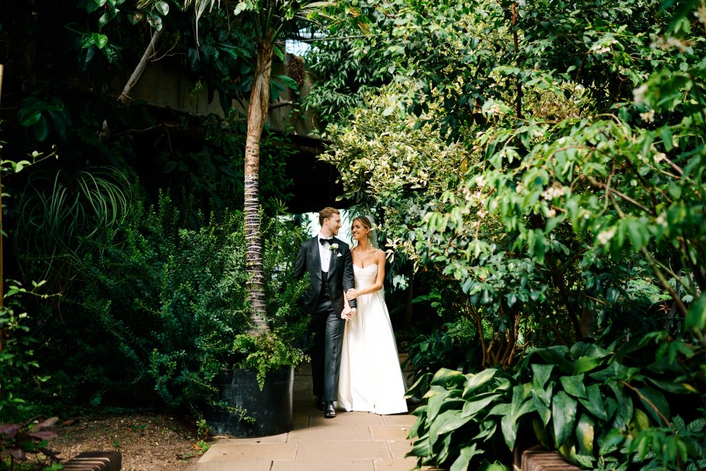 Bride and groom walking hand in hand through a leafy garden pathway